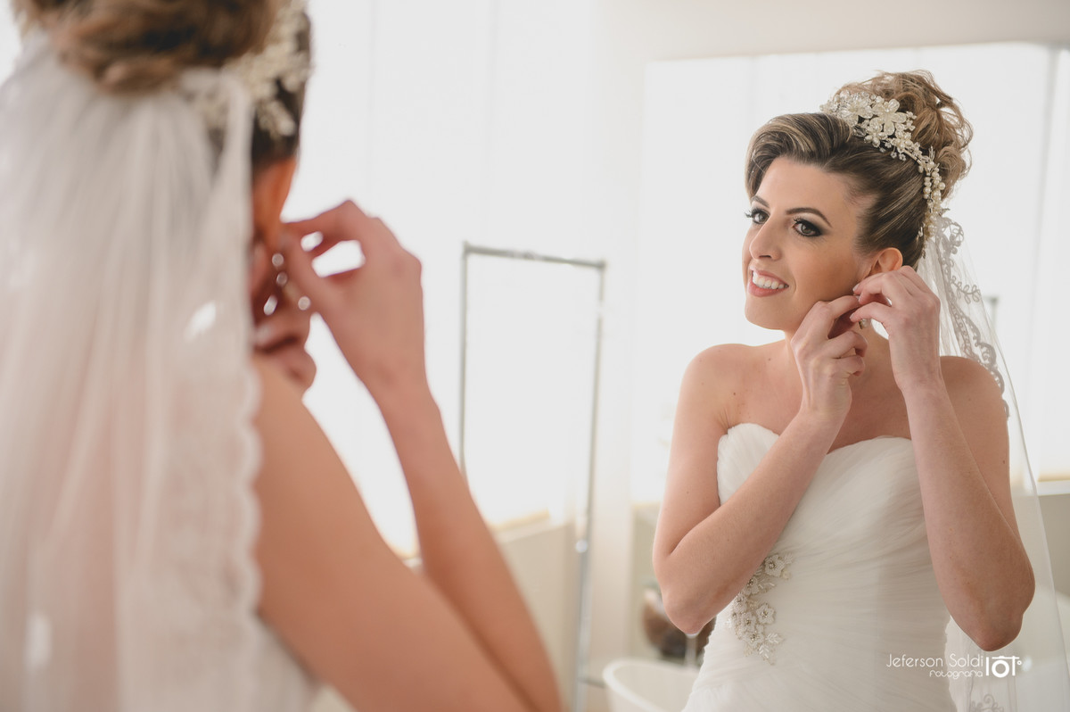 Noiva colocando os brincos em frente ao espelho.