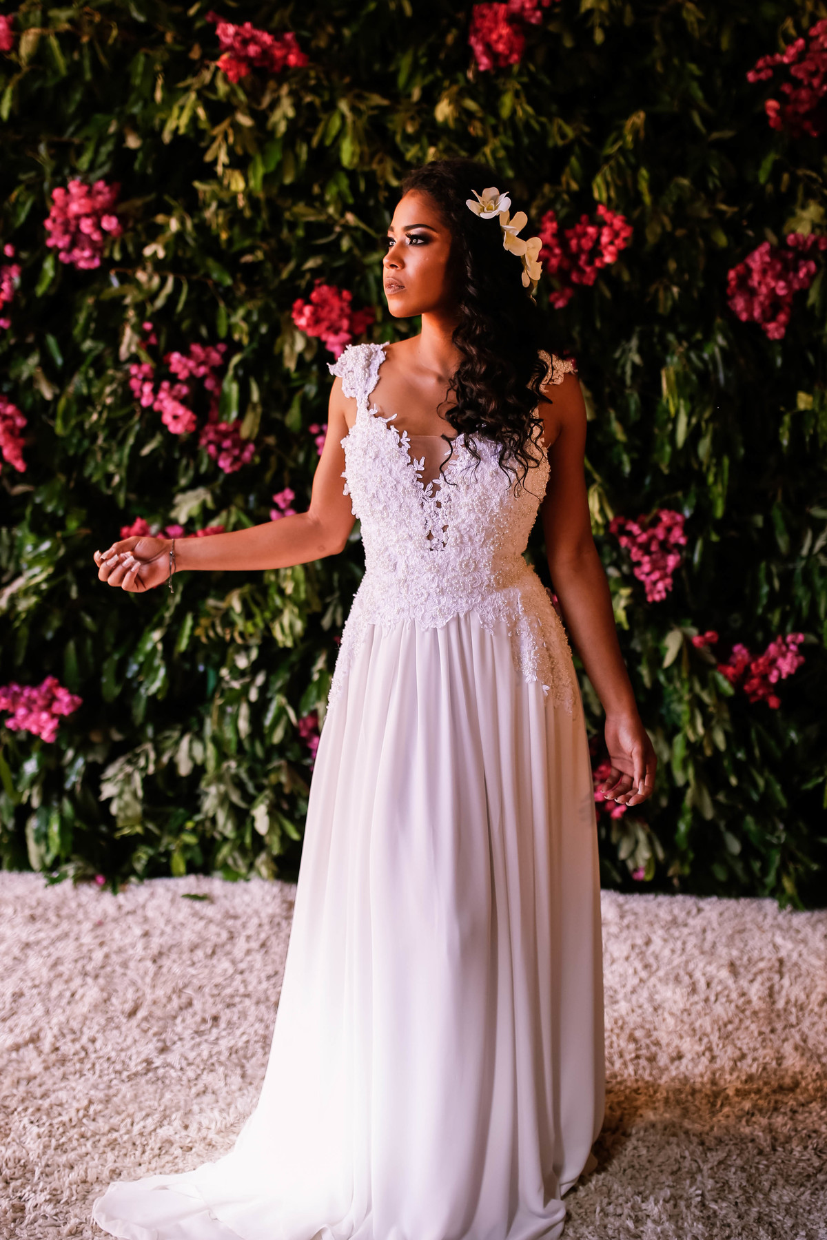 cacheada com vestido de noiva na frente de flores 