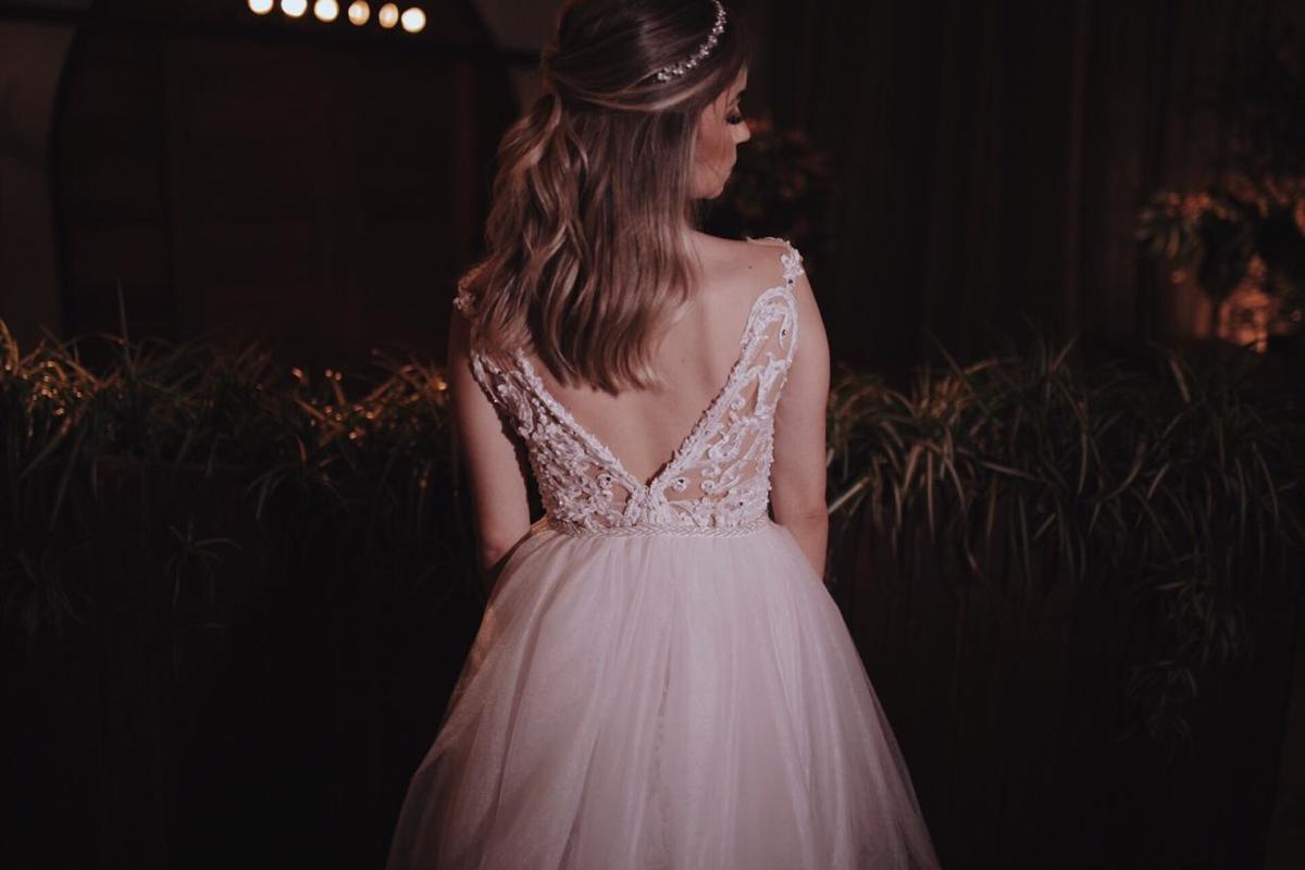 costas de uma loira com vestido branco em frente a flores