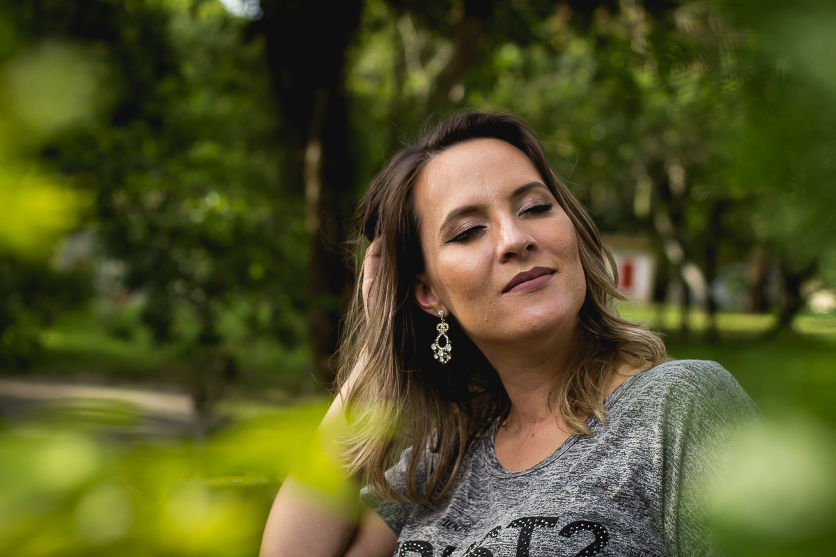 a gestante entre folhas verdes mexendo no cabelo e de olho fechado