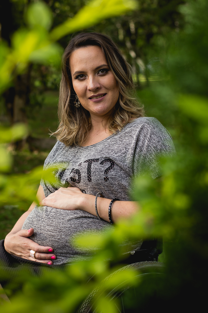 a gestante entre as folhas verdes com a mão na barriga e sorrindo