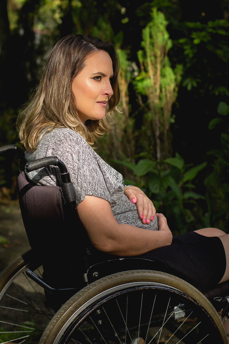foto na vertical da gestante com a mão na barriga sob um feixe de luz do sol