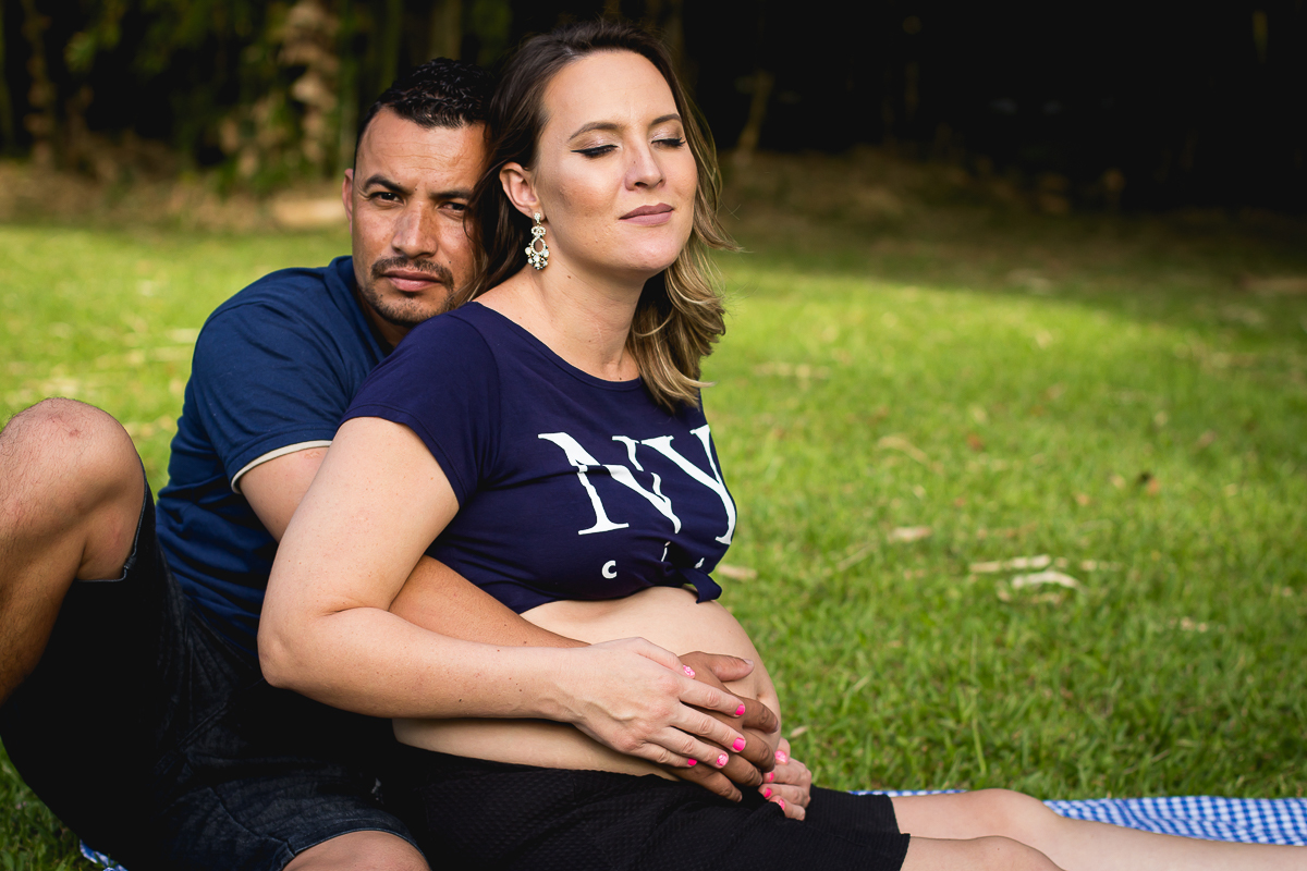 gestante de com o seu marido sentados em um gramado verde lindo