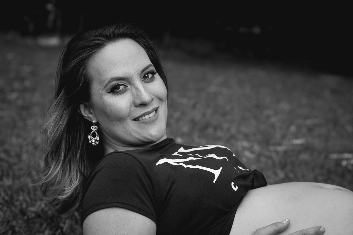 foto em preto e branco da gestante sorridente com os braços apoiado no gramado