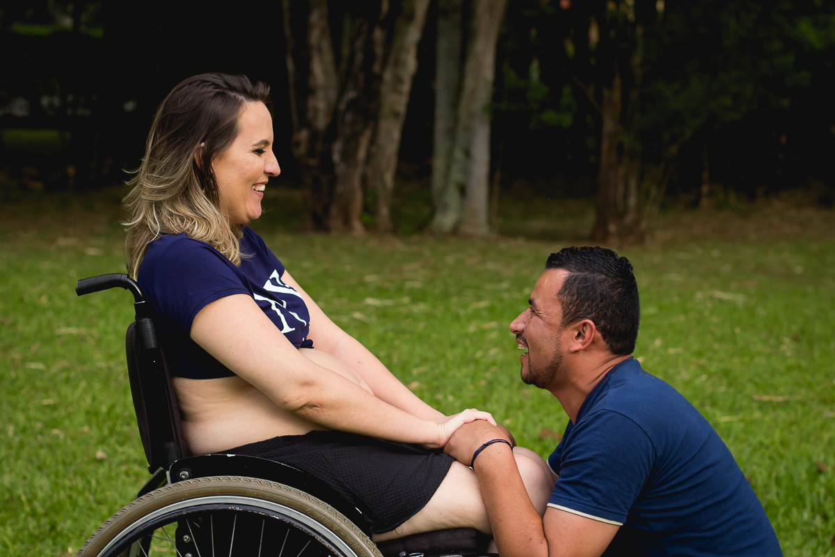 gestante na cadeira de roda de mão dadas com seu marido ajoelhado em sua frente e os dois sorrindo
