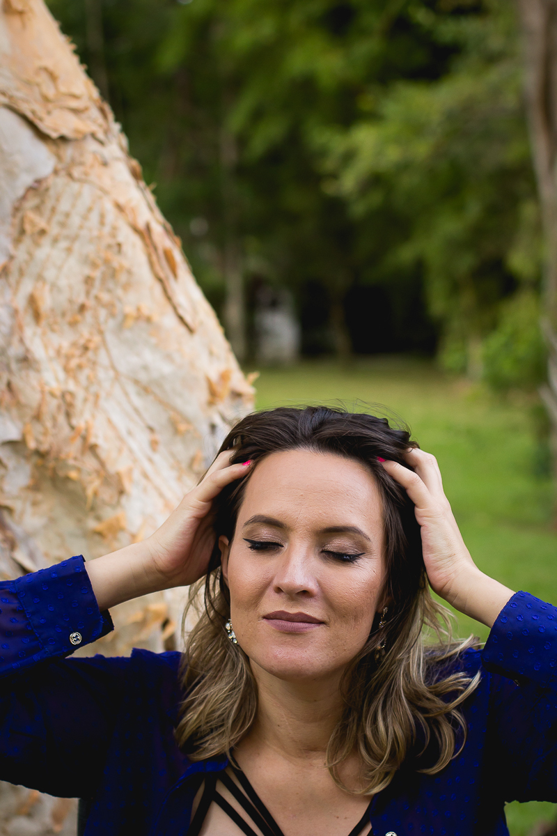 foto na vertical com a gestante de olhos fechados e com as duas  mãos nos cabelos