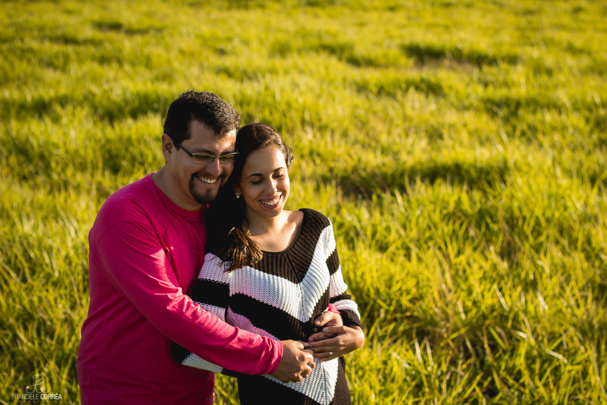 casal se abraçando e sorrindo de olhos fechados em um campo verde