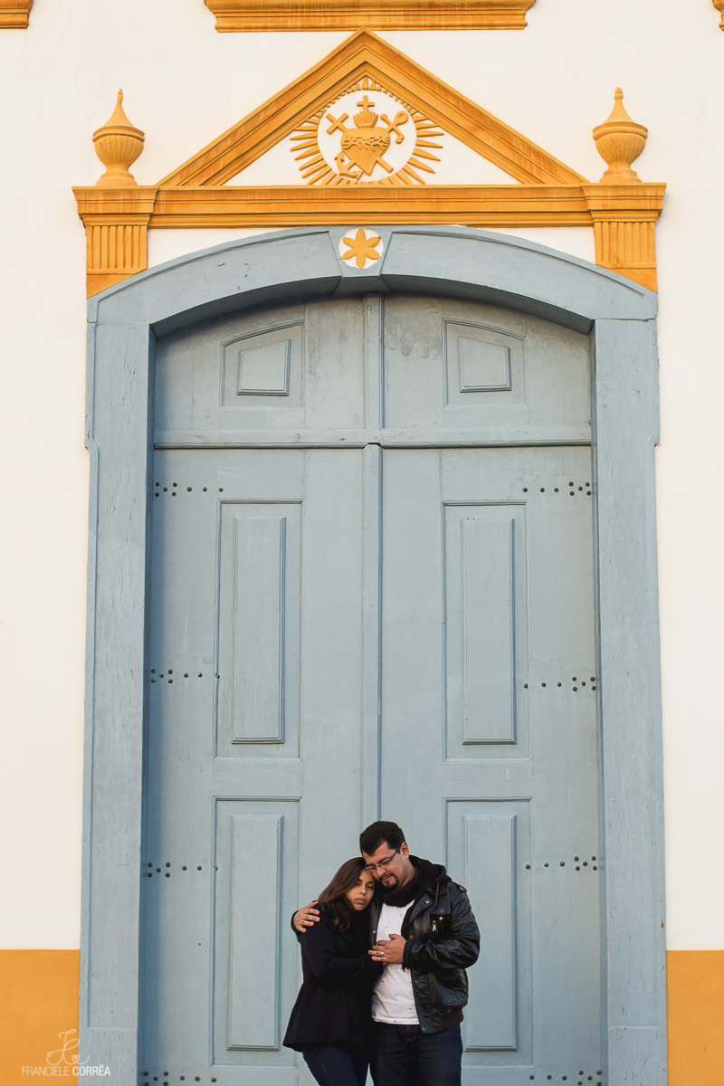 casal abraçados de olhos fechados em frente a porta de uma igreja