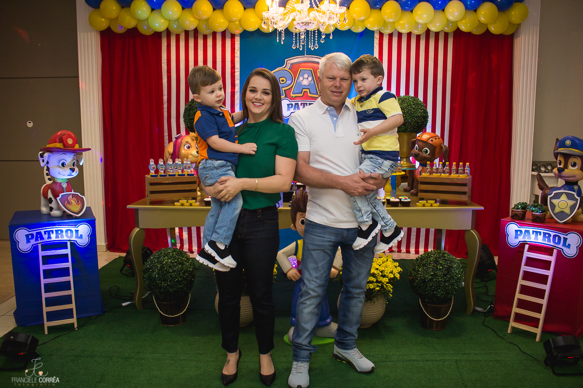 foto dos pais segurando os dois aniversariantes no colo em frente a decoração da festa