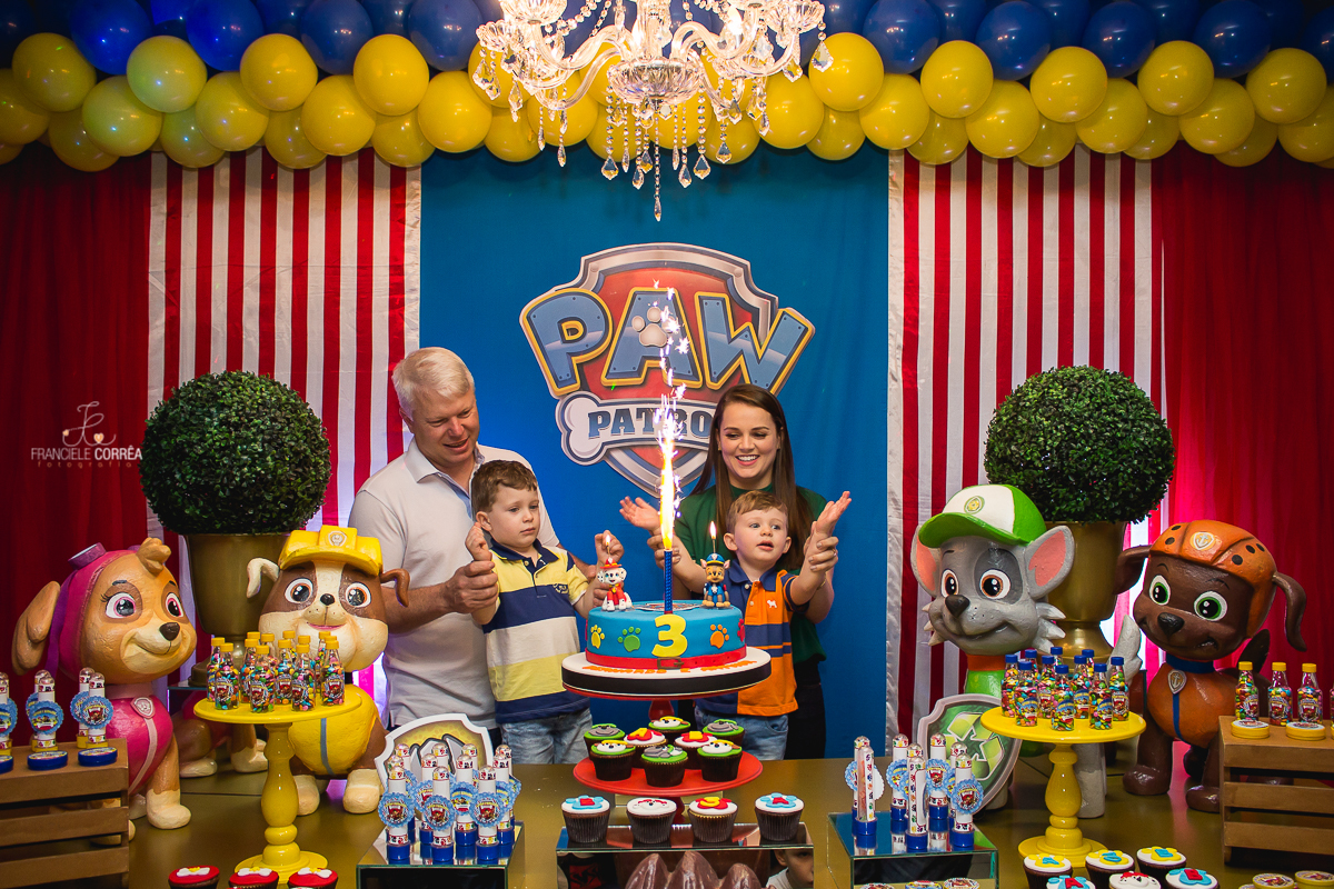 foto dos pais com os aniversariantes atrás do bolo na hora do parabéns com a vela chafariz acesa