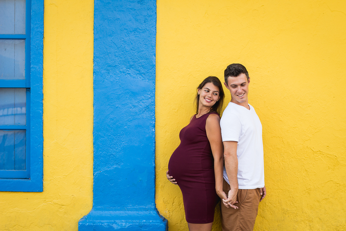casal de costa um para o outro de mãos dadas em frente a uma parede amarela