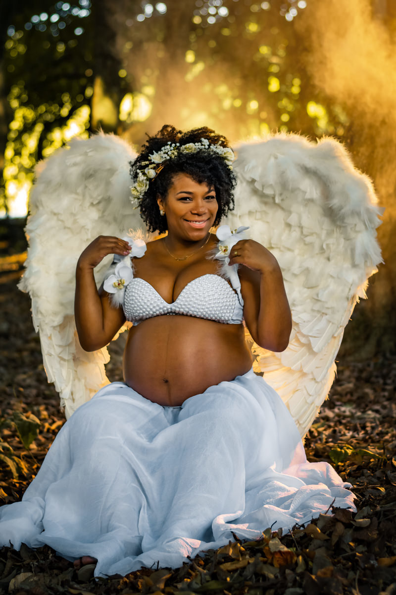 Mulher negra gestante com asas de anjo setada em meio a fumaça artificial, bosque da barra