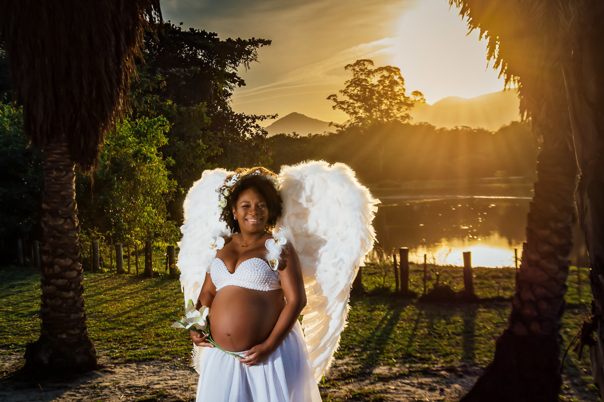 Mulher negra gestante usando asas de anjo na beira de um lago num belo final de tarde ao por do sol no Bosque da Barra
