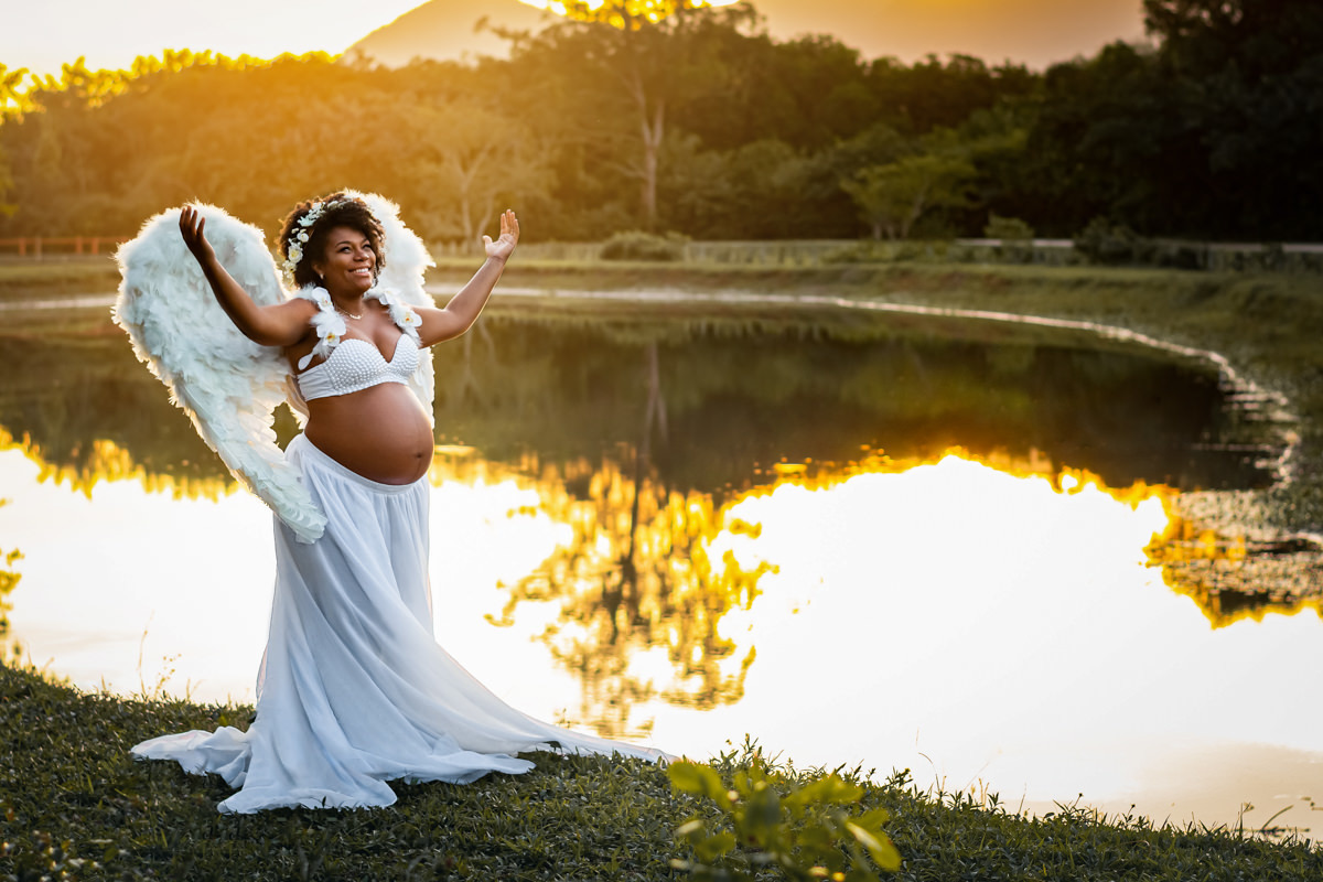 Mulher negra gestante usando asas de anjo na beira de um lago num belo final de tarde ao por do sol no Bosque da Barra
