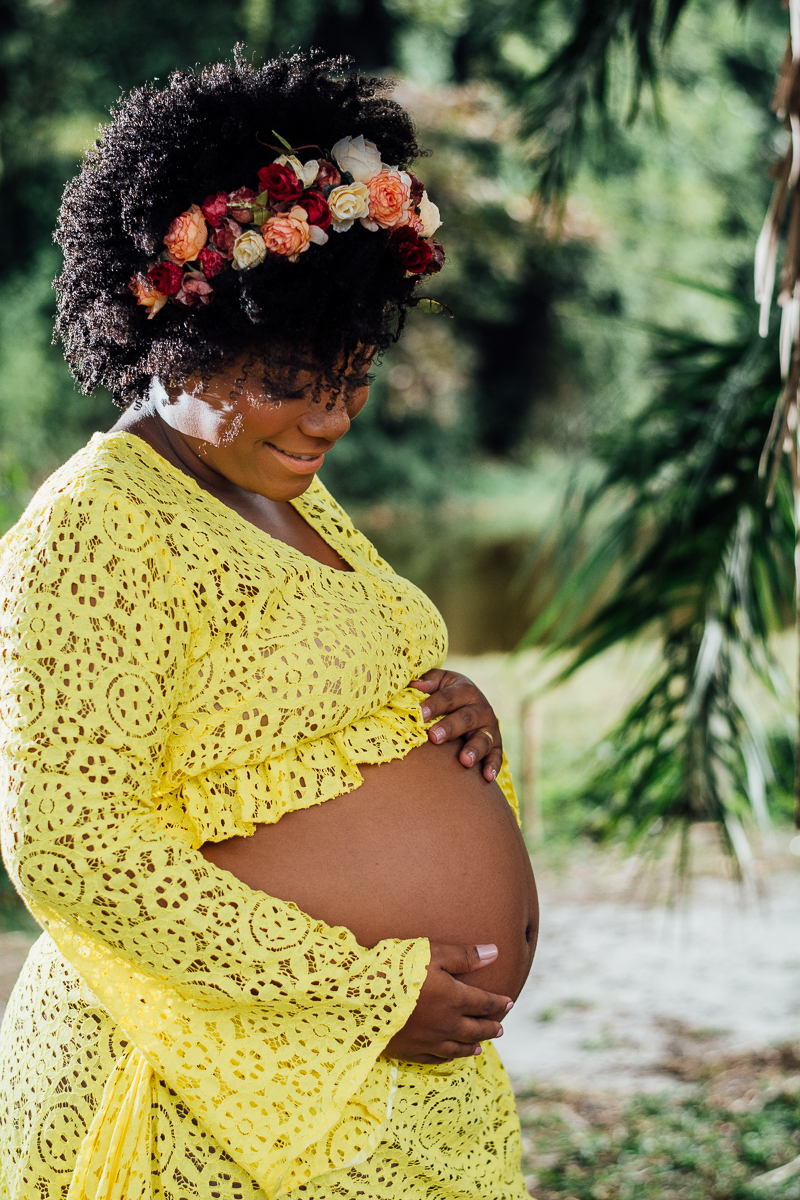 Mulher negra gestante usando vestido de renda amarelo e coroa de flores