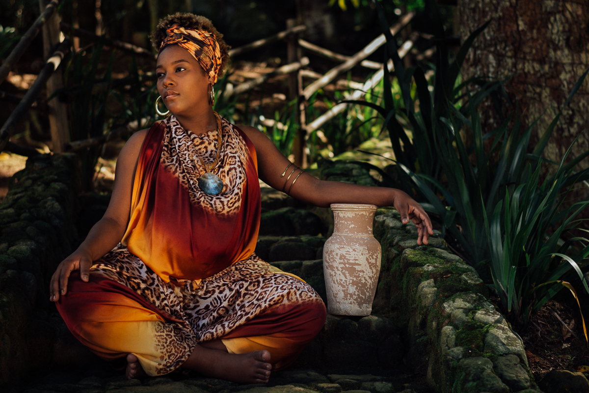 Gestante negra com vestido de estampa africana sentada na escada com um barro de jarro
