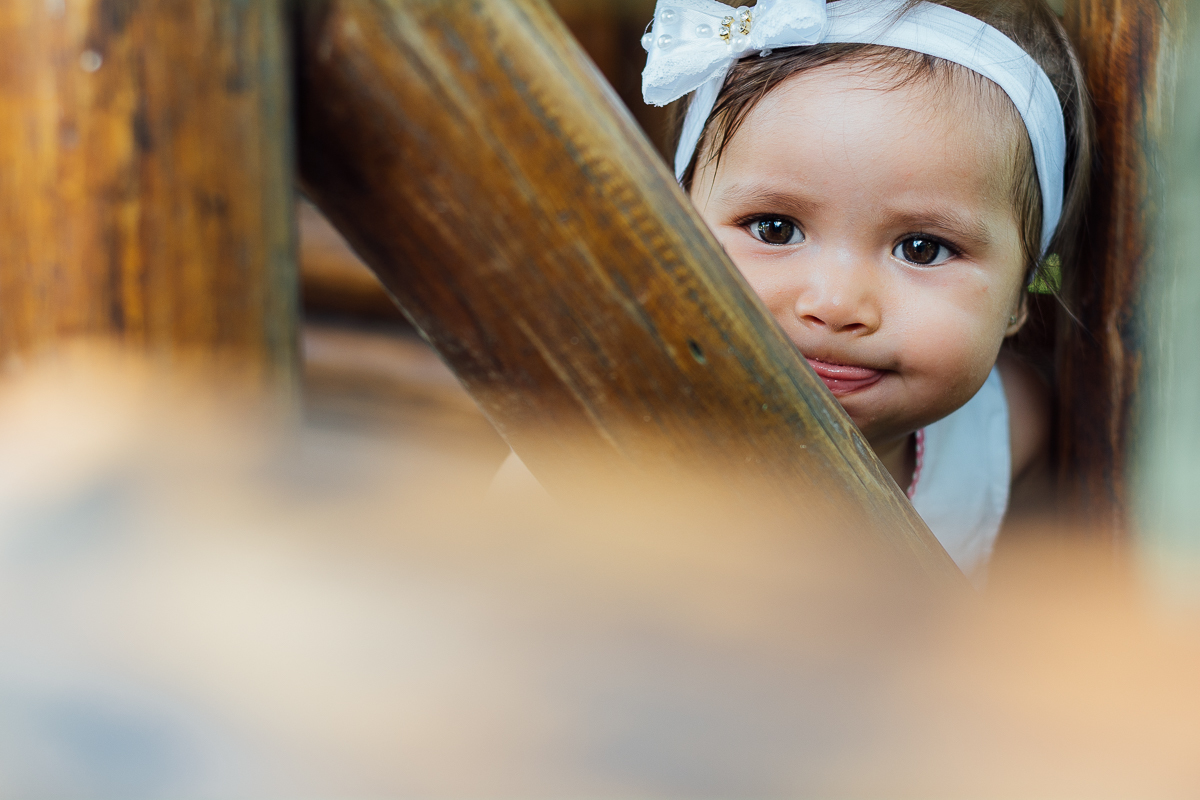Bebê menina de vestido estampado e laço branco na cabeça brincando de esconder na casinha de madeira