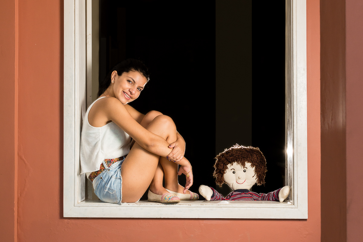 Menina sentada na janela com o boneco de infância