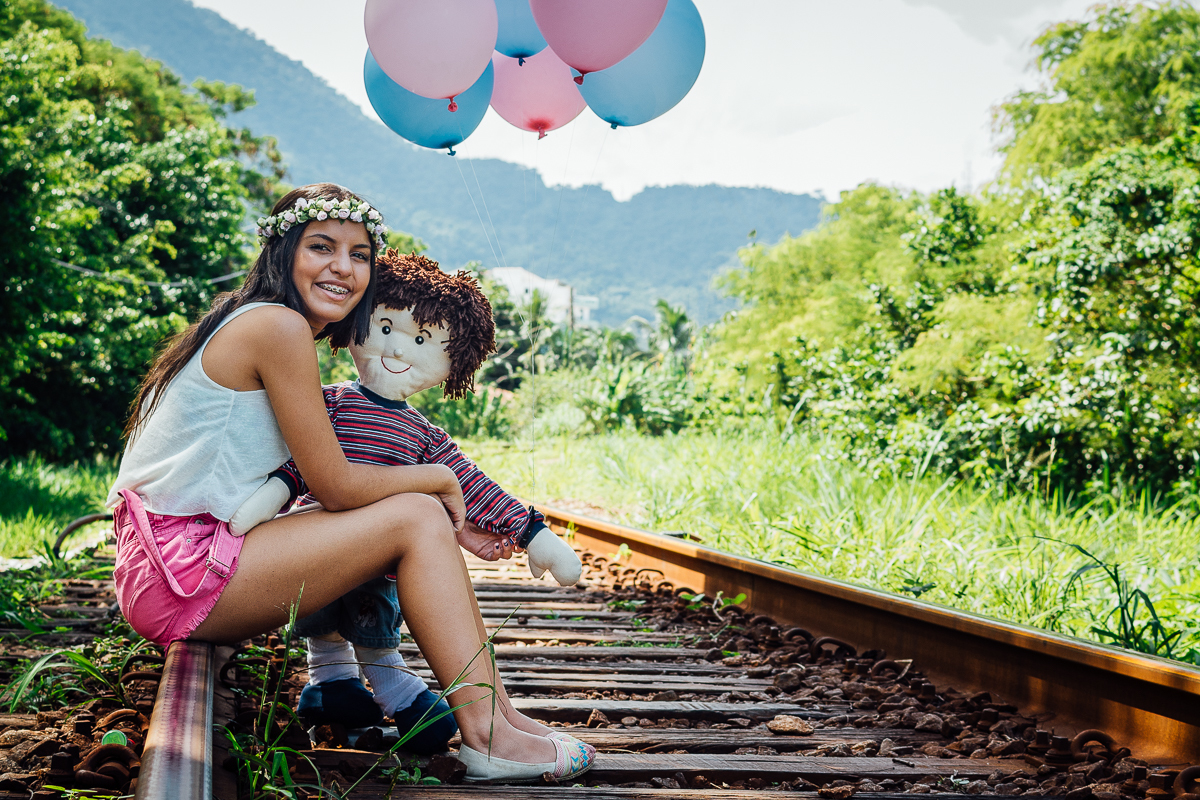 Menina sentada na linha do trem com o boneco de infância e bolas de gás
