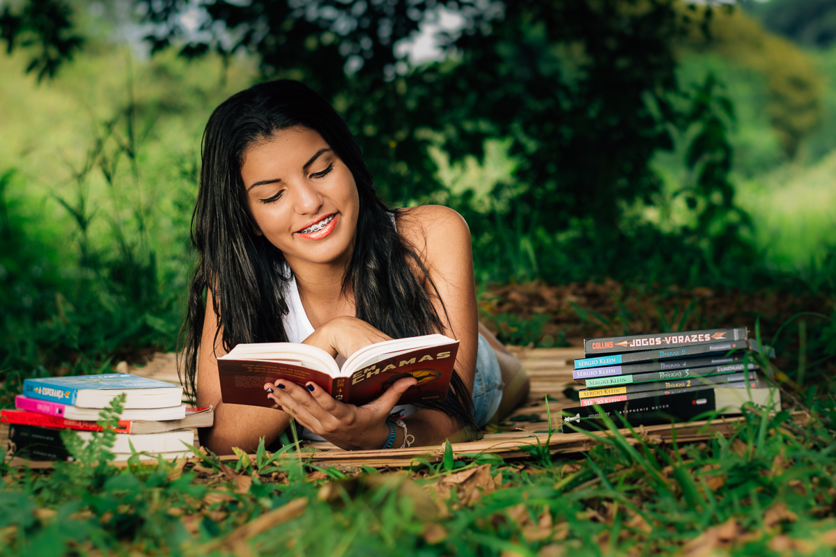 Menina lendo livro deitada de baixo da arvore