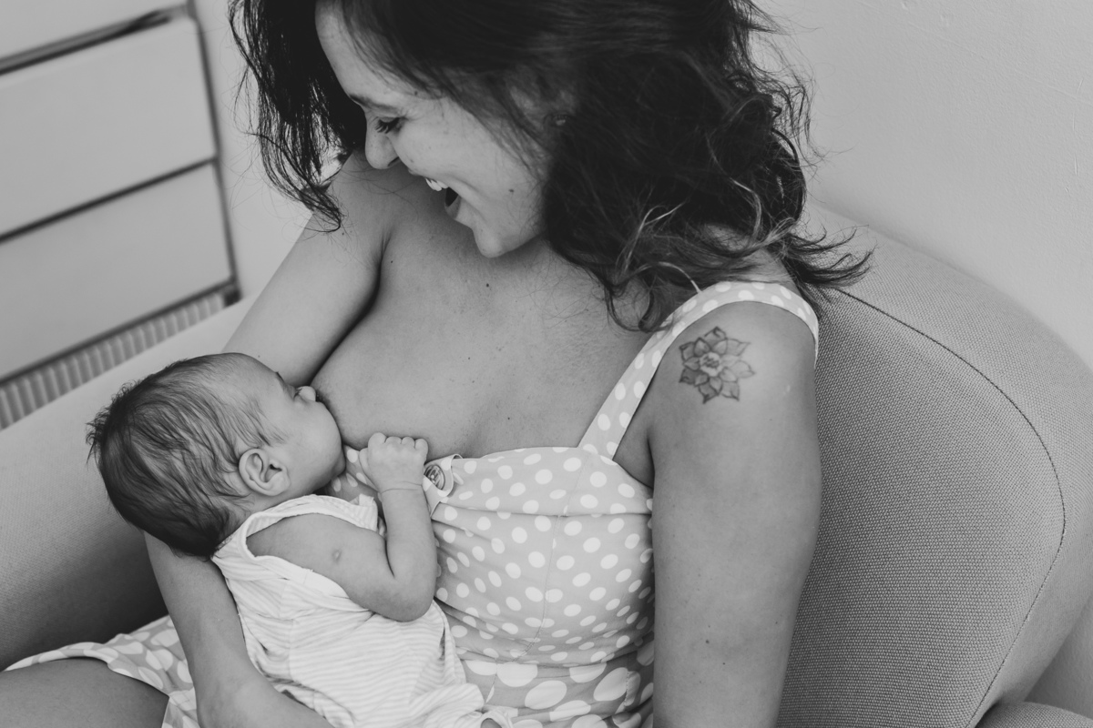 Mamãe sorridente sentada na cadeira ou sofá de amamentação, da mama para o bebê