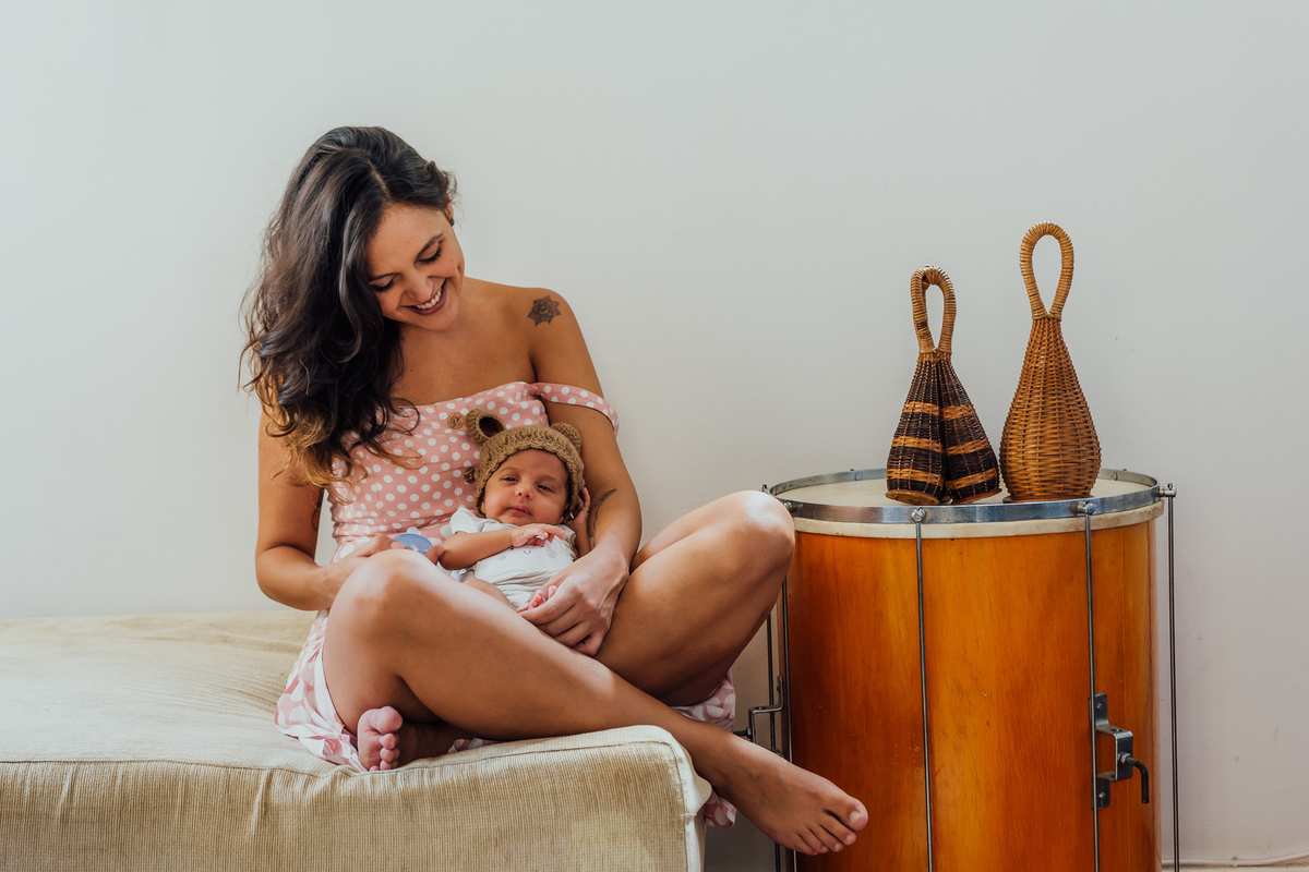 Mamãe sentada no sofá da sala, com o bebê entre suas pernas, ao lado de instrumentos musicais