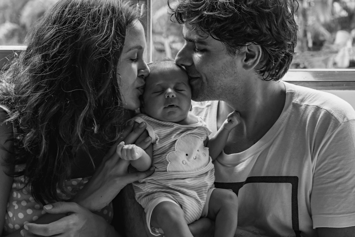Papai e mamãe dão chuva de beijos no bebê
