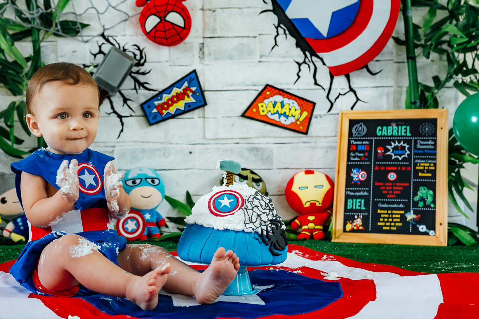 bebê fantasiado de capitão america no ensaio cake smash com o tema vingadores bebê  lambusado de bolo e batendo palmas, bolo do capitão america