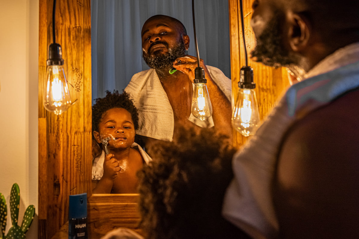 Pai e filho em frente ao espelho com moldura de madeira, o pai ensina a fazer a barba.