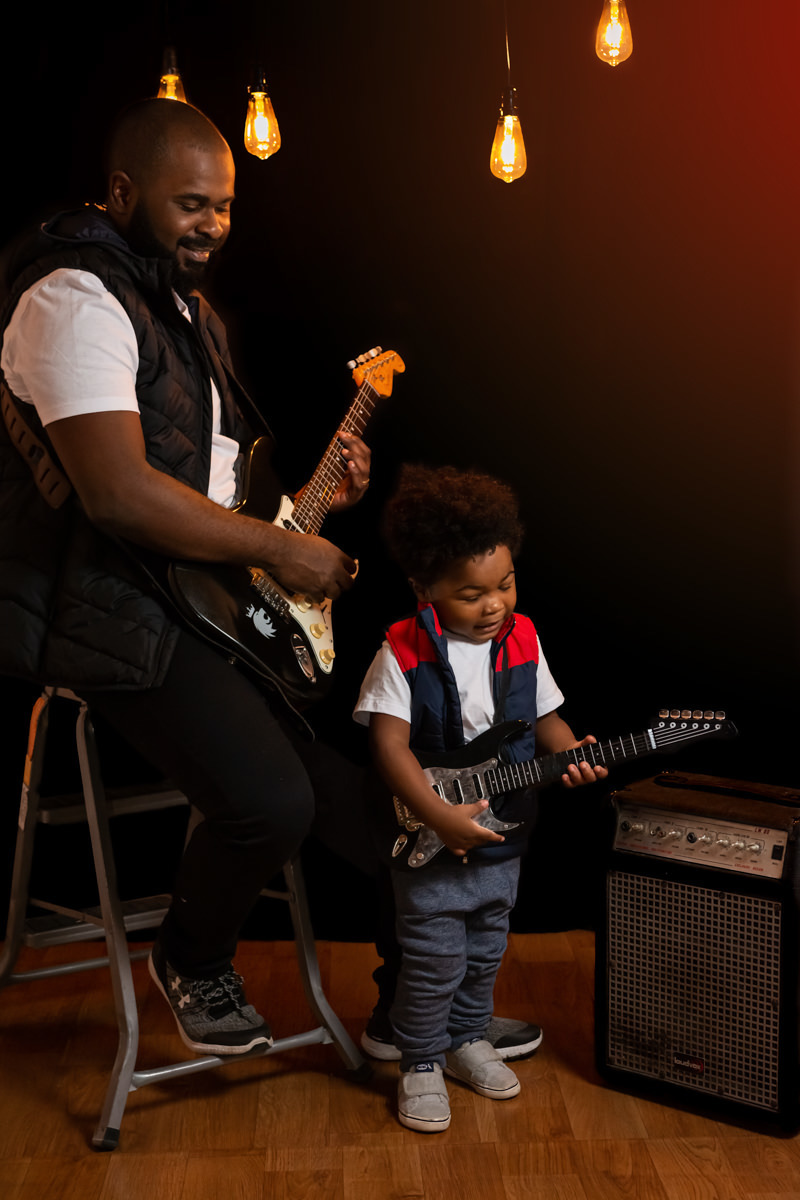 Pai e filho cantando, o pai tocando baixo e o filho guitarra,