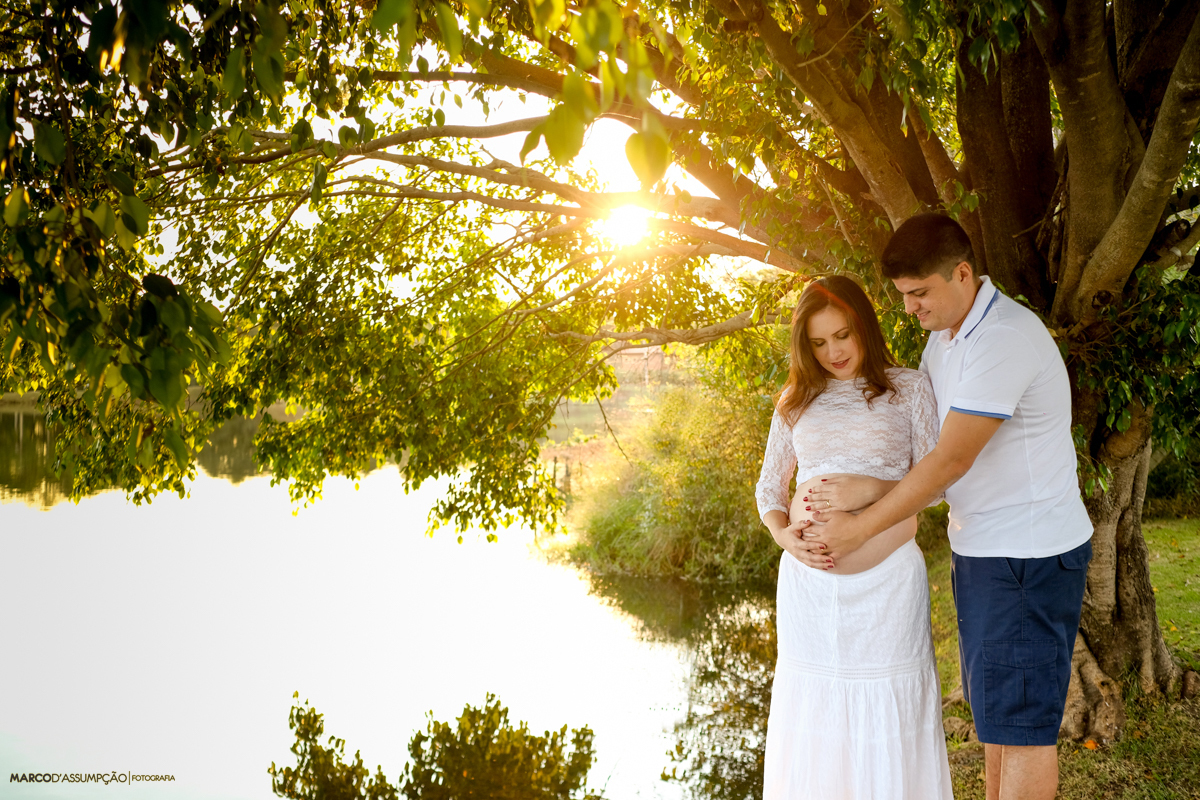 casal olhando para barriga da gestante no lago com por do sol em indaiatuba