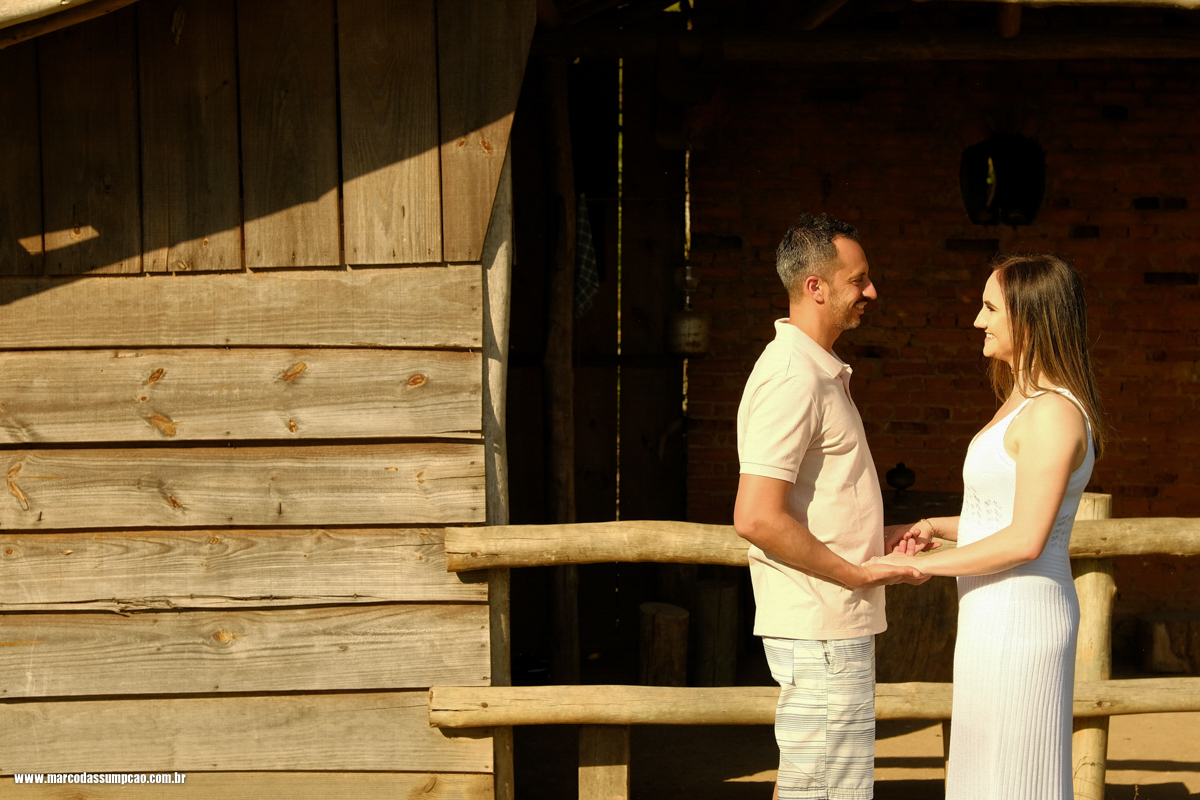 casal de maos dadas se olhando em frente a rancho de fazenda
