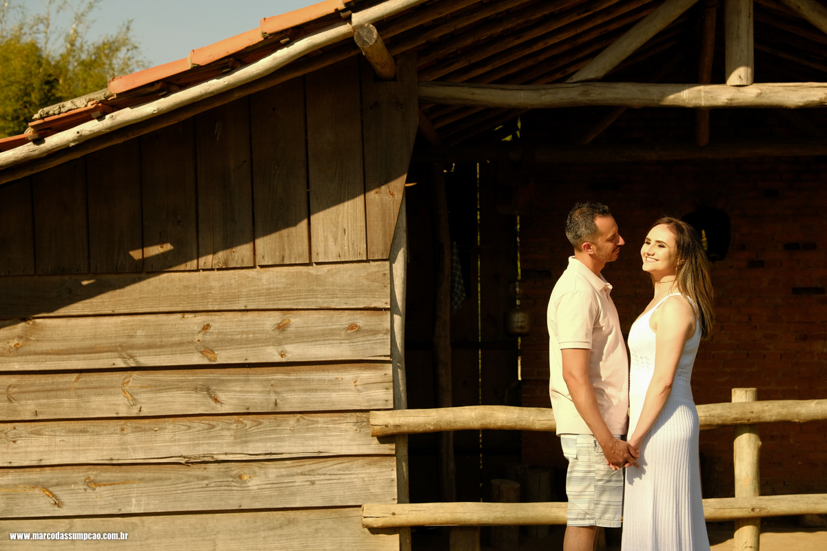 casal de maos dadas sorrindo em frente a rancho de fazenda