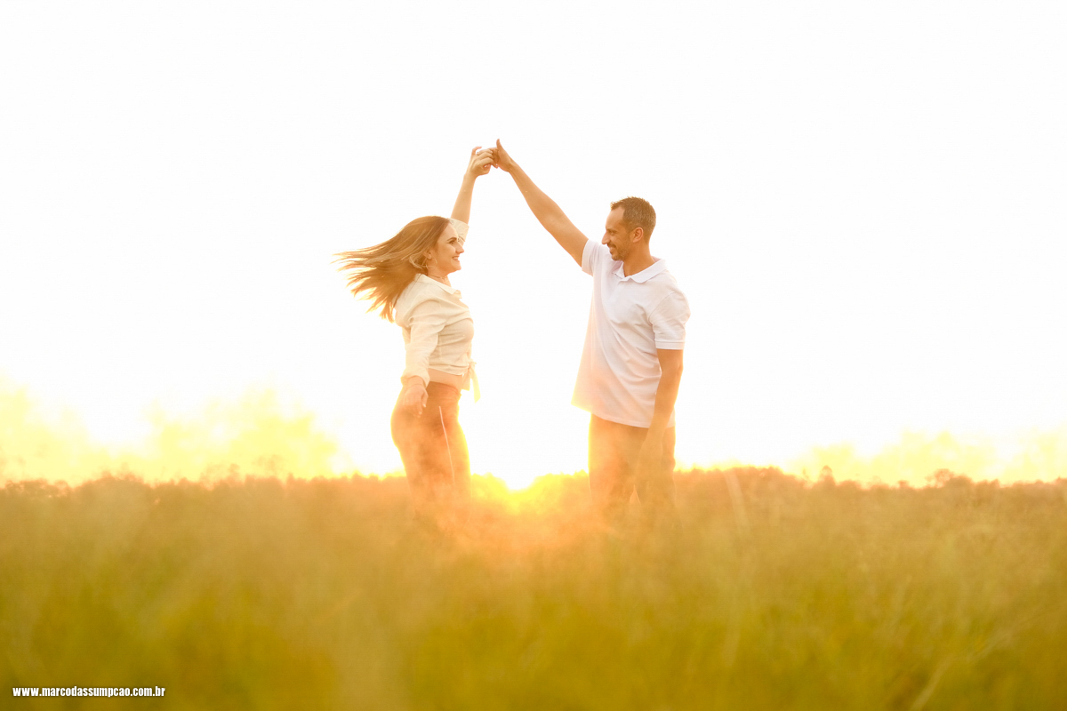 casal dancando no meio do feno em fazenda com por do sol ao fundo