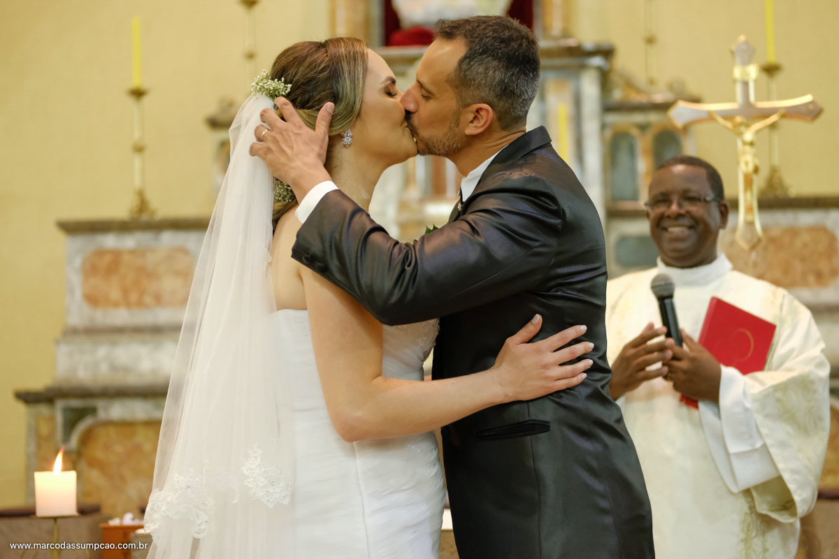 noivos se beijando no altar ao final da cerimonia com celebrante sorrindo