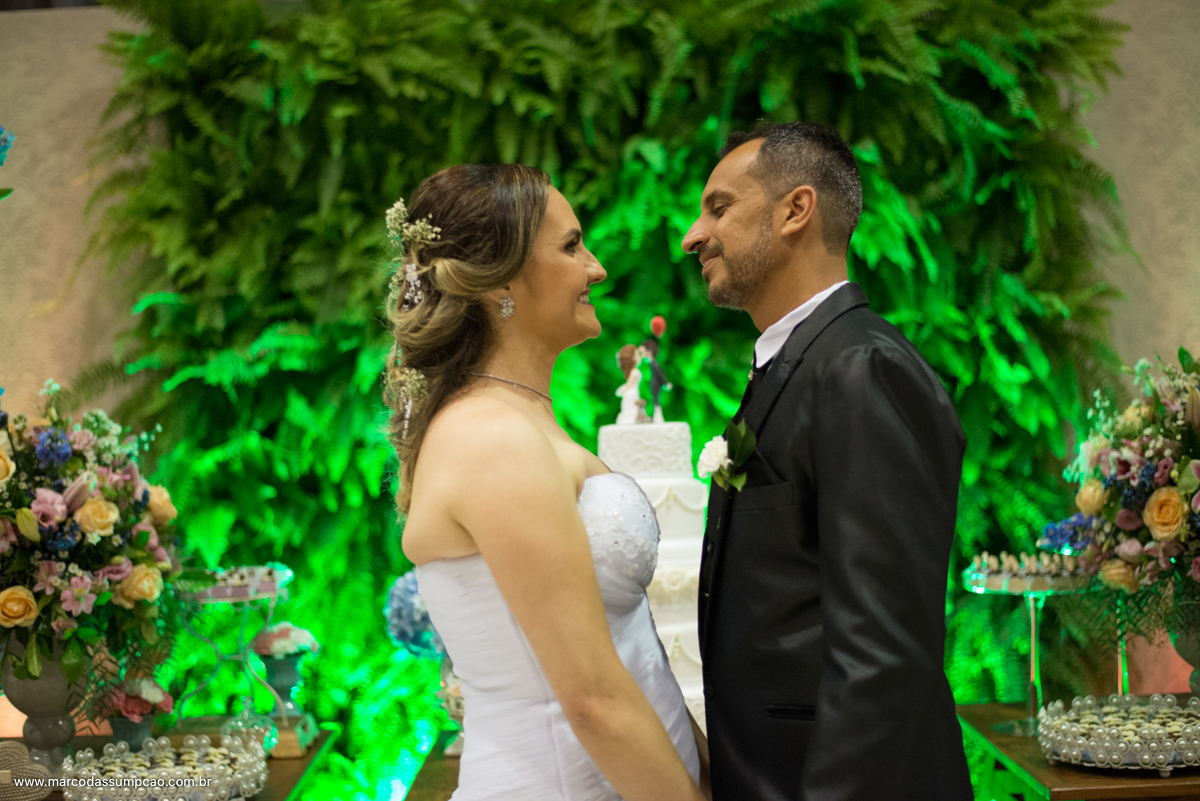 noivos em frente a mesa de bolos se olhando
