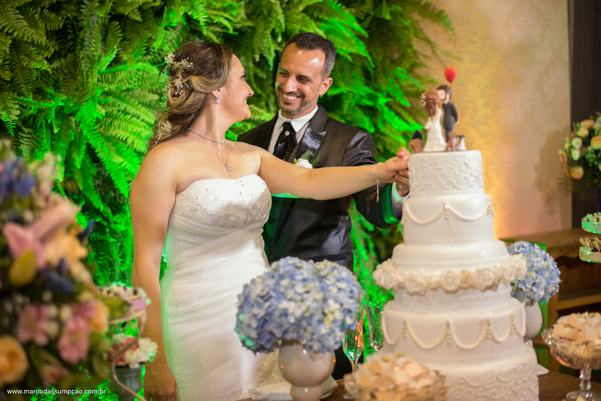 noivos se olhando e cortando o bolo de casamento com plantas verdes ao fundo