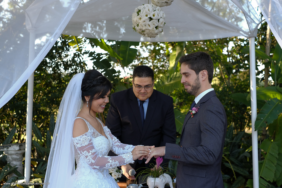noiva colocando as aliancas na mao do noivo e sorrinso