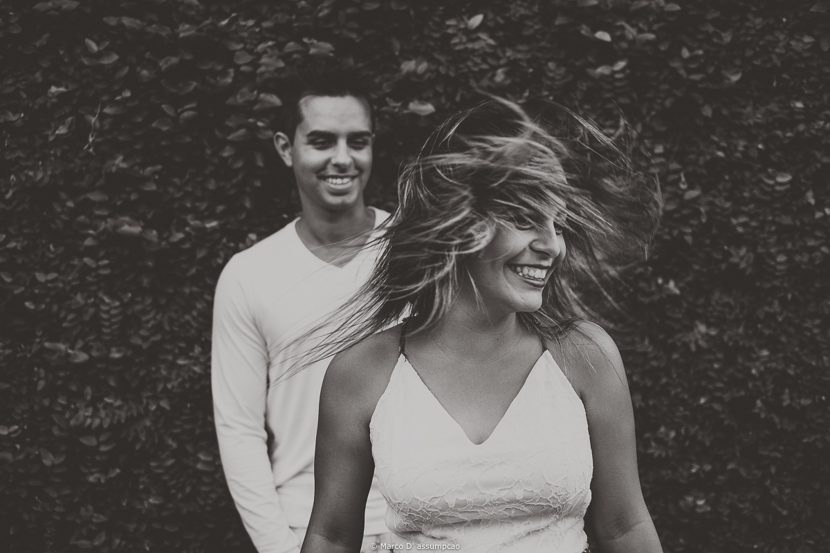 noiva jogando o cabelo para os lados e sorrindo com noivo ao fundo