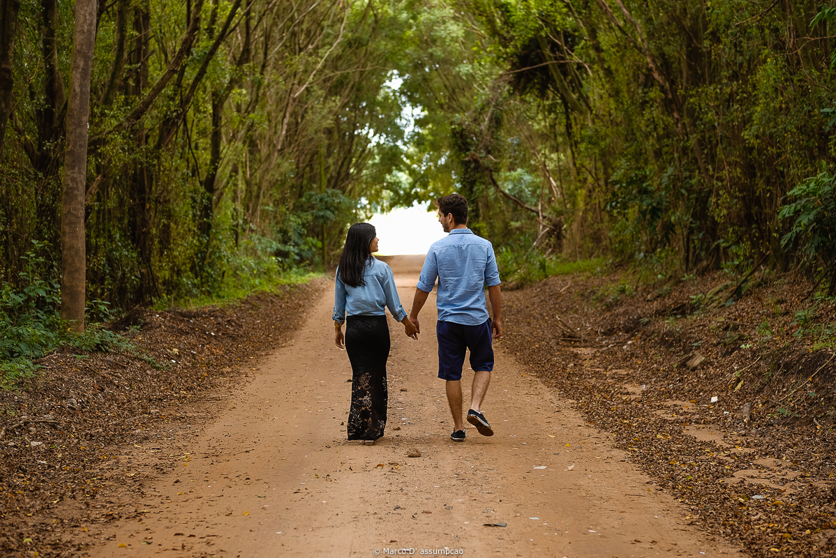 casal andando de costas em meio a arvores e estrada de terra