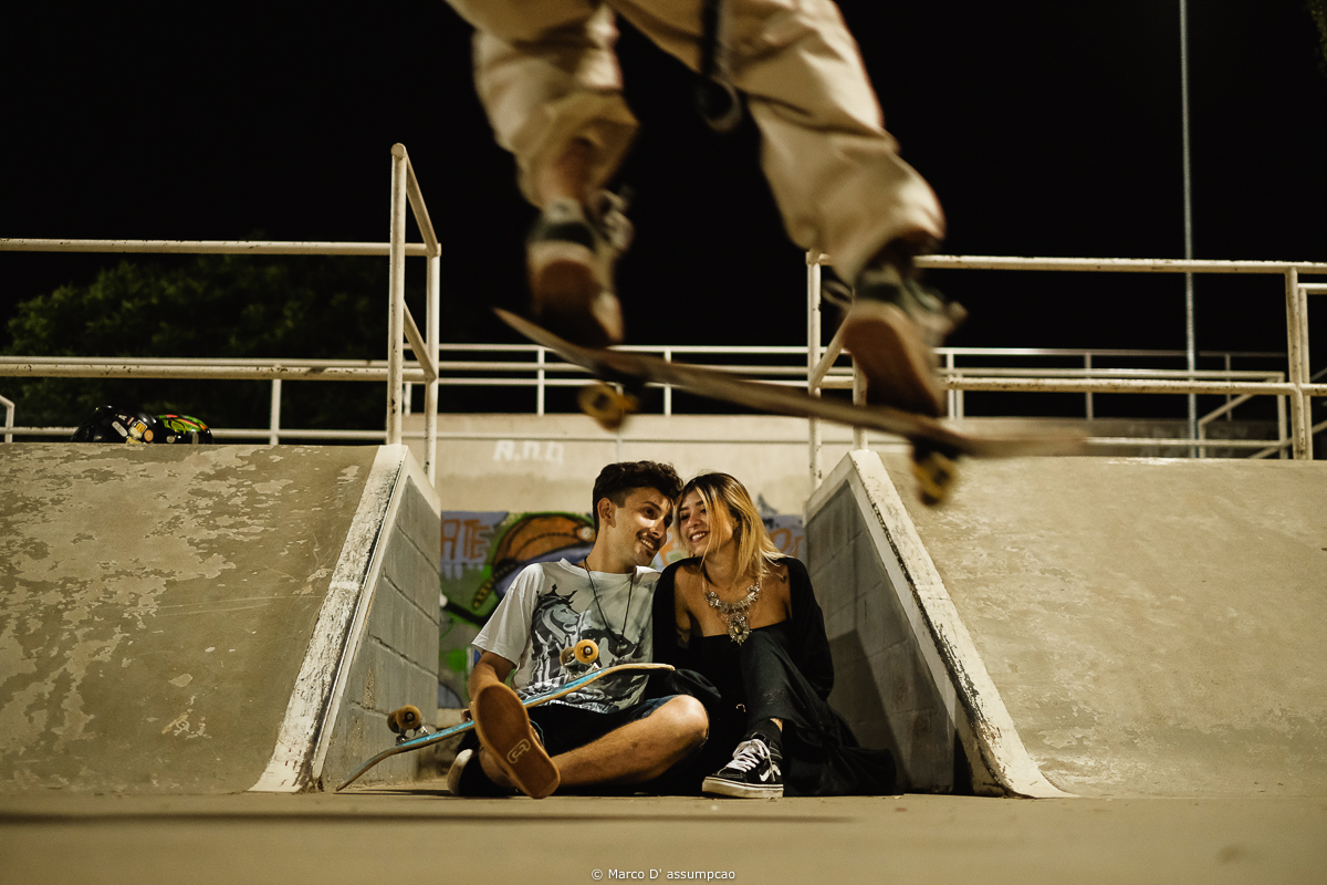 casal sentado no chao com skate passando por cima