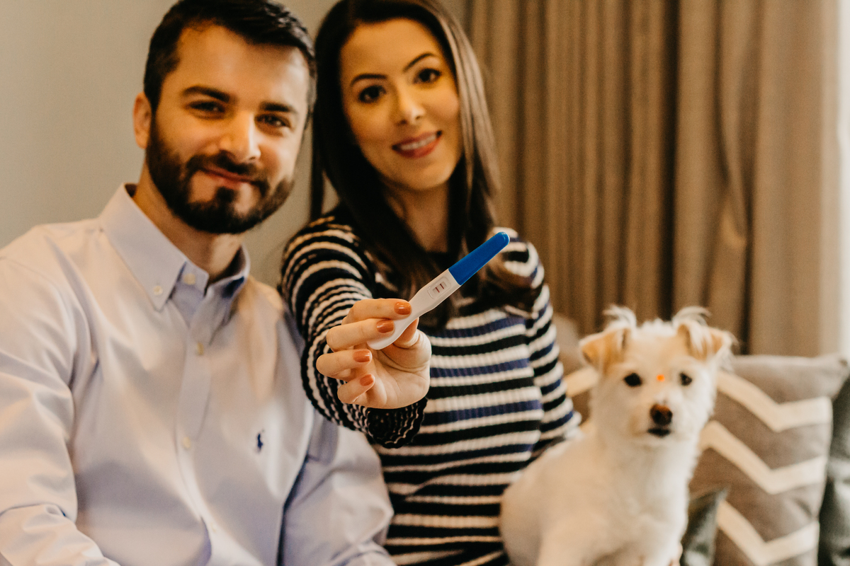 casal mostrando teste de gravidez positivo com cachorro no colo, sentados no sofa