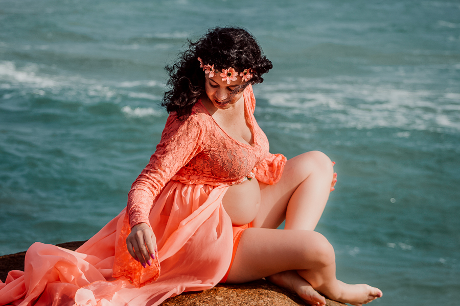 Gestante vestido sentada sobre a rocha, mar ao fundo na praia do rosa.

