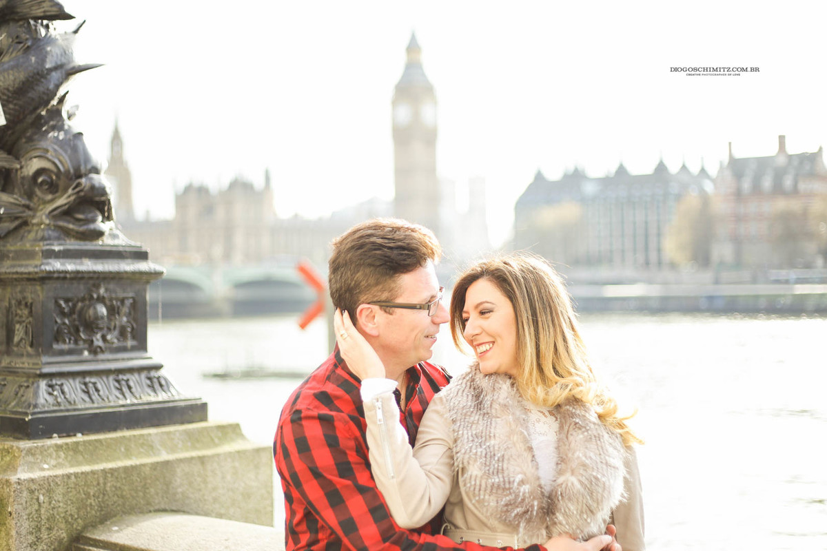 Casal se abraçando e sorrindo em frente ao Palácio de Westminster.
