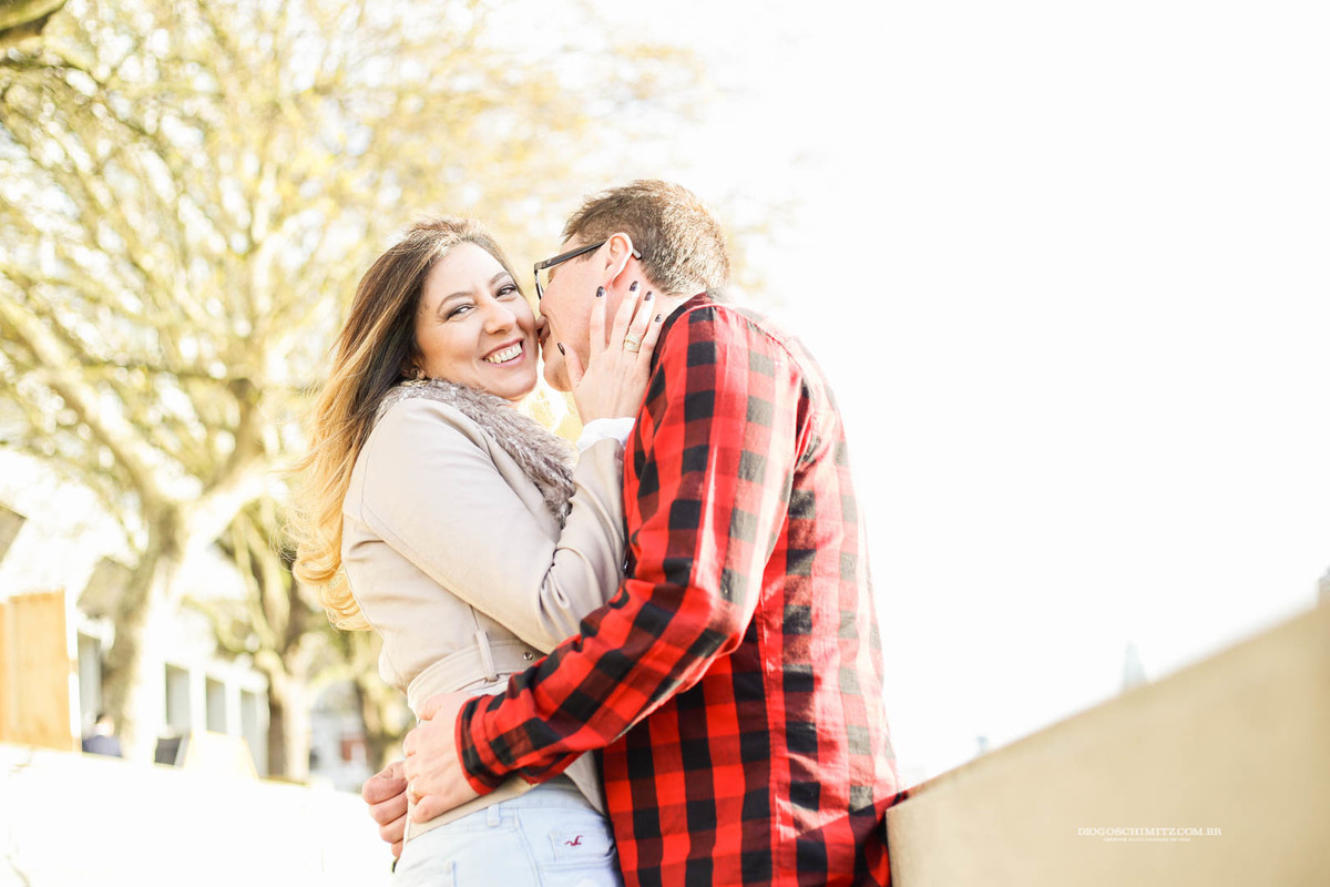 Homem beijando o rosto da mulher enquanto ela olha para o lado e sorri.