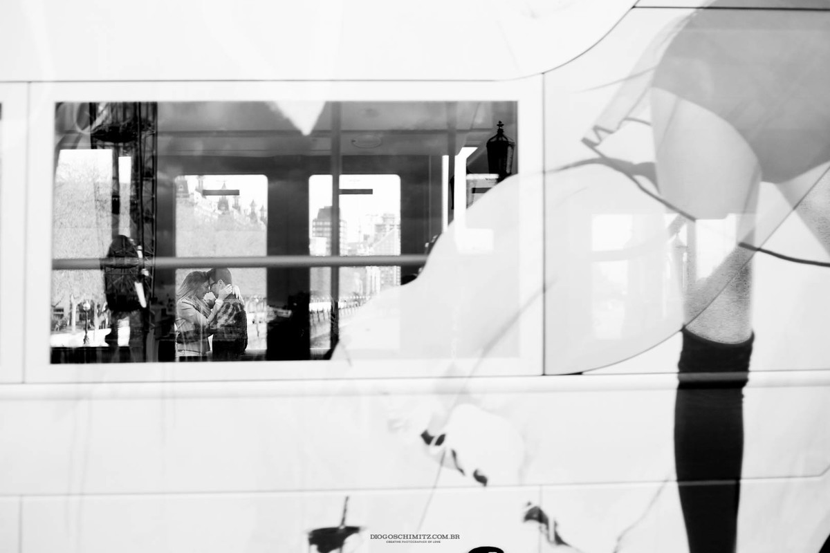 Casal se abraçando enquanto um ônibus passa em frente a câmera.