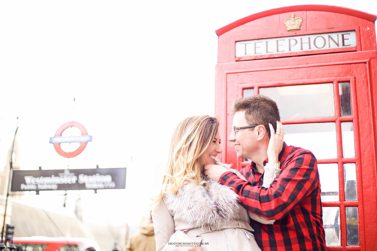 Casal se divertindo em frente a uma cabine telefônica.