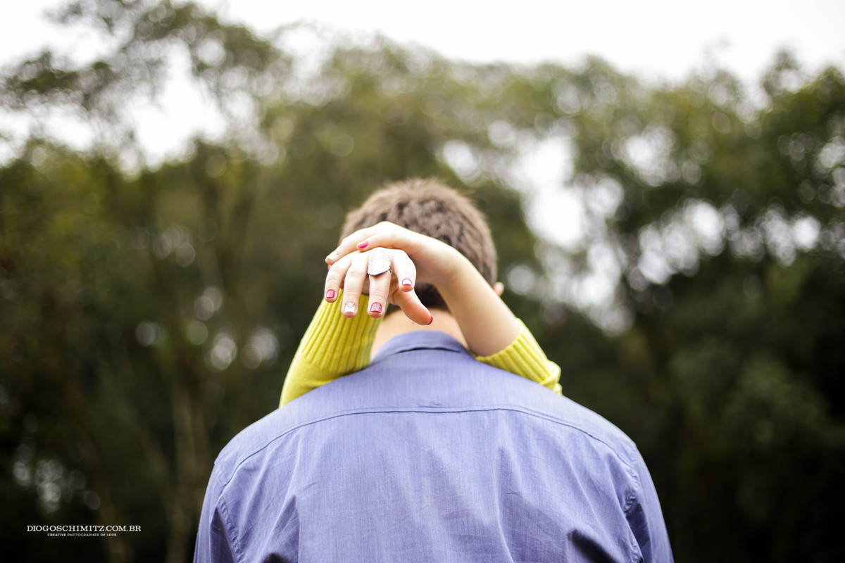 Homem de costas com os antebraços da mulher apoiados em seus ombros.
