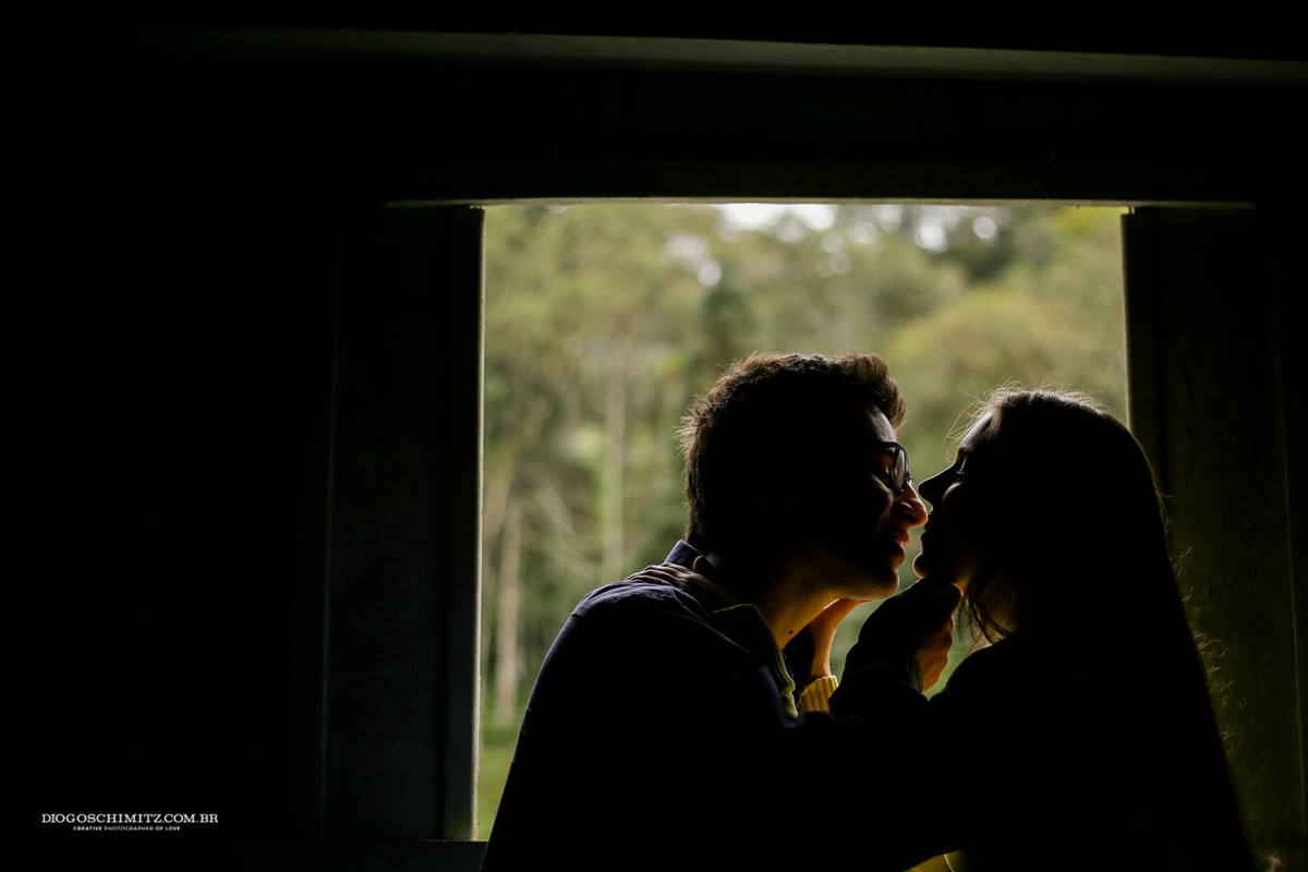 Casal se beijando em frente a uma janela.