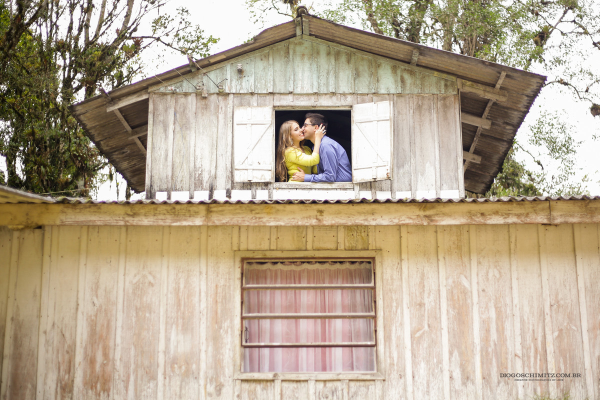 Homem beijando o rosto da mulher em frente a uma janela.
